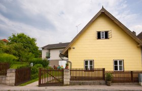 Vorderansicht, © srad Ein gelbes Haus mit Spitzdach und Holzzaun in einer ländlichen Umgebung.