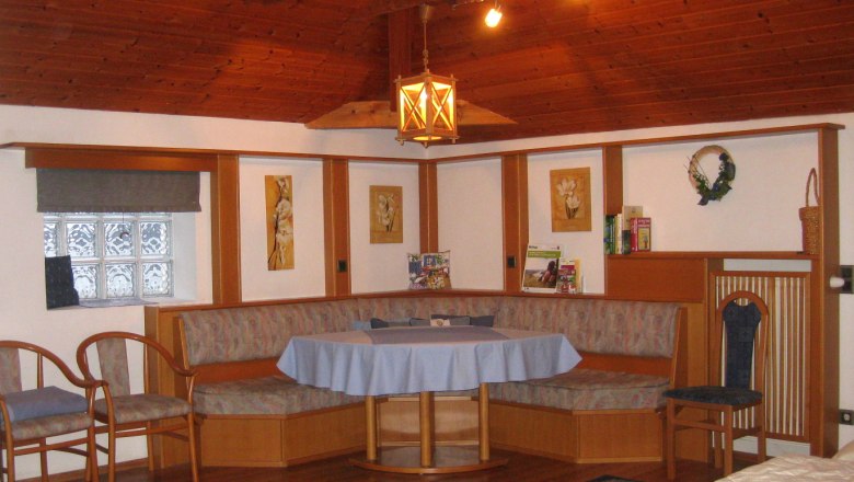Zimmer 2, © Kienesberger Gemütliche Sitzecke mit Holzmöbeln und blauer Tischdecke in einem Raum mit Holzdecke.