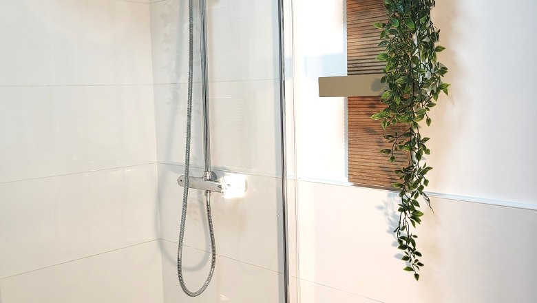 Dreimäderlhof, © Helga und Thomas Kraushofer Dusche mit Regenduschkopf, daneben ein Regal mit Pflanzen und Handtüchern.