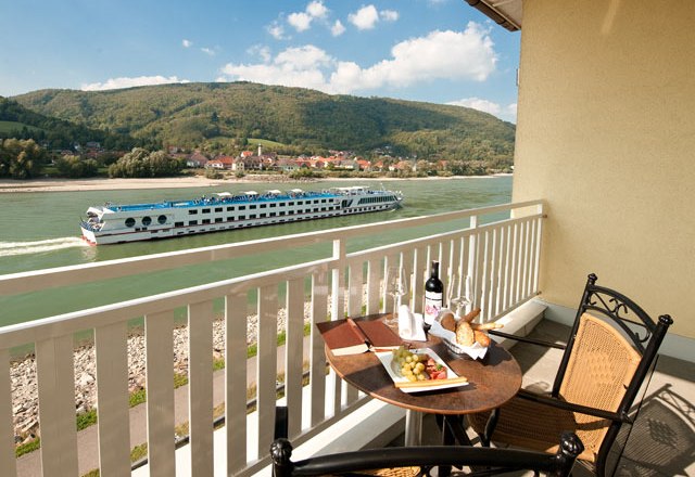 Aussicht Suite, © Residenz Wachau Balkon mit Tisch, Wein und Snacks, Blick auf Fluss und vorbeifahrendes Schiff.
