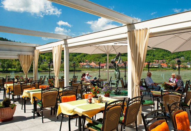 Restaurantterrasse, © Residenz Wachau Restaurantterrasse mit Blick auf einen Fluss und grüne Hügel im Hintergrund.