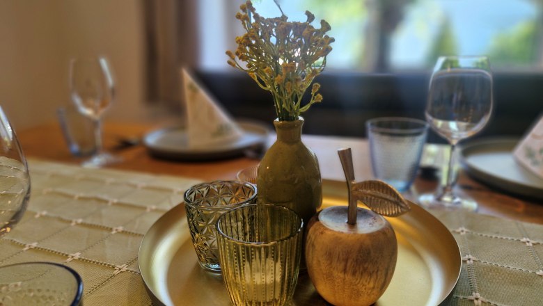 Dreimäderlhof, © Helga und Thomas Kraushofer Ein dekorativer Tisch mit einem goldenen Tablett, auf dem eine Vase mit Blumen, zwei Gläser und ein hölzerner Apfel stehen.