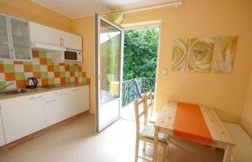 Helle Küche mit Essecke, bunter Fliesenspiegel und offener Balkontür.