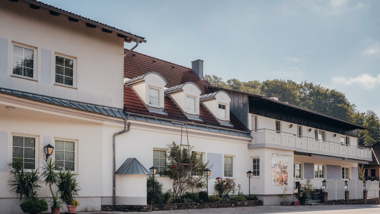 Ein zweistöckiges Gebäude mit weißen Wänden und roten Dachziegeln, umgeben von Pflanzen und Laternen.