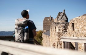 Ein Wanderer mit Rucksack betrachtet die Burgruine Aggstein an einem sonnigen Tag.