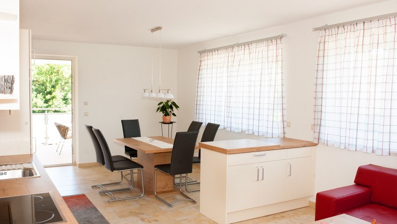 Moderner Essbereich mit Holztisch, schwarzen St&uuml;hlen und gro&szlig;en Fenstern mit Vorh&auml;ngen.