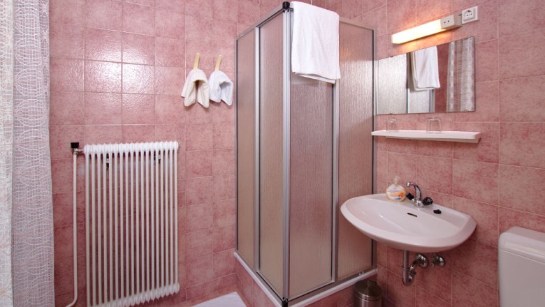 Badezimmer mit rosa Fliesen, Duschkabine, Waschbecken und Heizkörper.