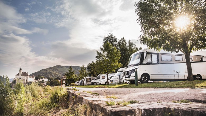 Wohnmobile auf einem Campingplatz mit Schloss im Hintergrund.