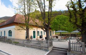 Außenansicht eines gelben Gebäudes mit rotem Dach und Biergarten.