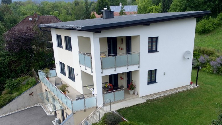 Drohnenaufnahme eines modernen zweist&ouml;ckigen Hauses mit Balkon und Garten.