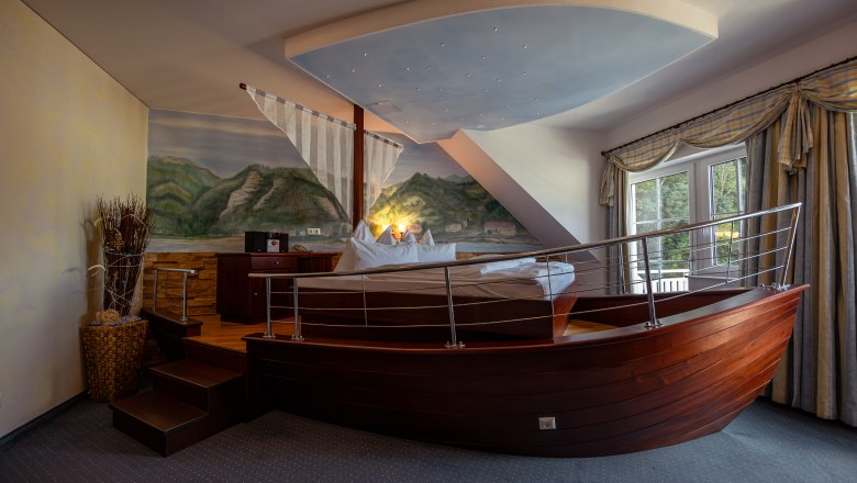 Hotelzimmer mit Bett in Form eines Bootes, Wandgemälde von Landschaft, Fenster mit Vorhängen.